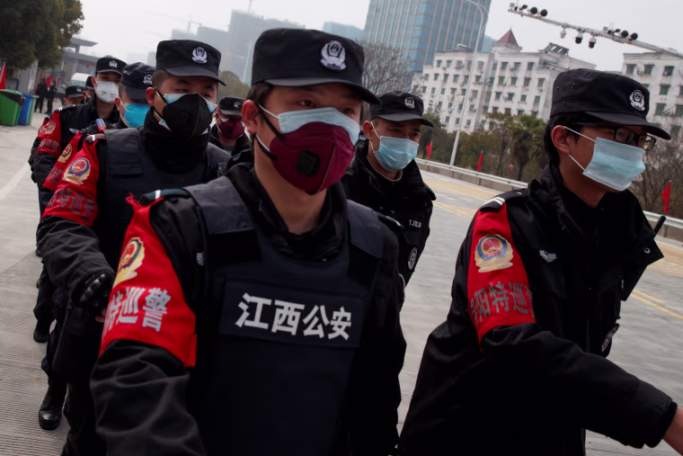 Image: Security guards walk in formation for a shift change at a checkpoint to the Hubei province exclusion zone at the Jiujiang Yangtze River Bridge in Jiujiang
