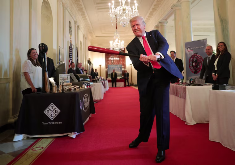Image: President Trump swings a wooden baseball bat as he attends a \"Spirit of America Showcase\" event in the Cross Hall of the White House in Washington