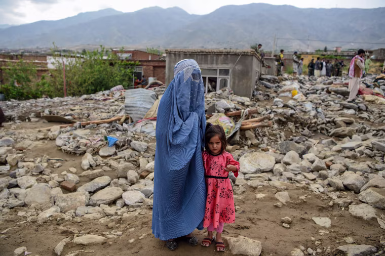 Image: A burqa-clad woman stands near a young girl among households' debris after a flash flood affected the area at Sayrah-e-Hopiyan in Charikar, Afghanistan