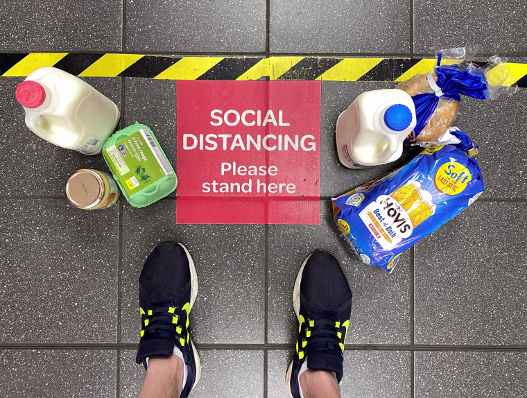 Image: Food shopping next to a social distancing sign at a British supermarket in April.