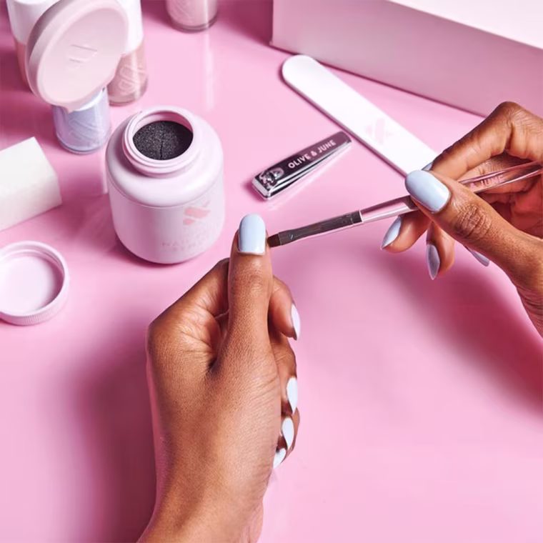 Woman giving herself a manicure using a Olive & June Manicure set