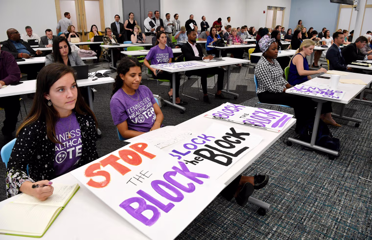 People from the Tennessee Justice Center hold signs at a public hearing on Oct. 1, 2019, in Nashville, Tenn., on Tennessee's request for block grant funding for Medicaid.