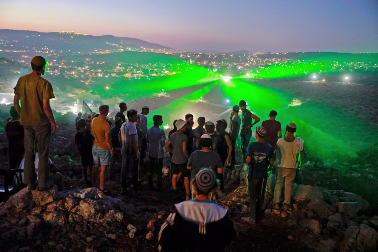 Israeli settlers in the outpost of Eviatar look on as Palestinian protestors flash laser beams towards them earlier this week. 