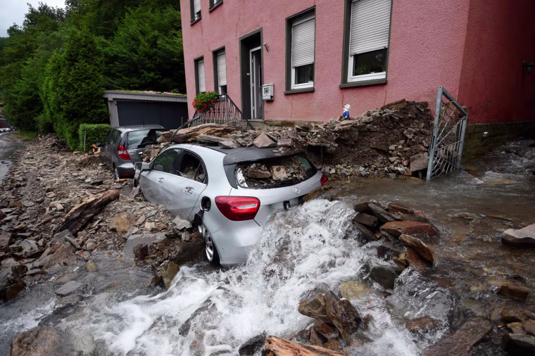 Water runs past a house with a car covered in rubble after heavy rain and floods caused major damage in Hagen, western Germany, on July 15, 2021.