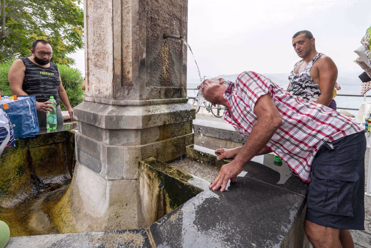 Image: A man refreshes himself in a fountain during a hot summer day in Messina, Sicily, Italy
