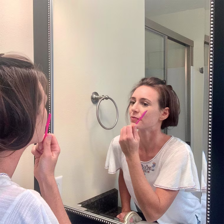Writer Katie Jackson looking in the mirror, using a small blue face razor