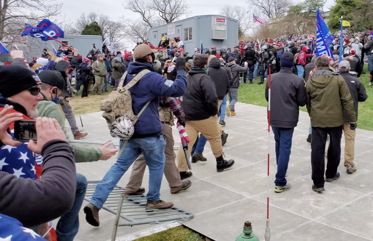 Image: Derek Kinnison, wearing a blue sweatshirt, steps on a police barrier as he approaches the Capitol on Jan. 6, 2021.