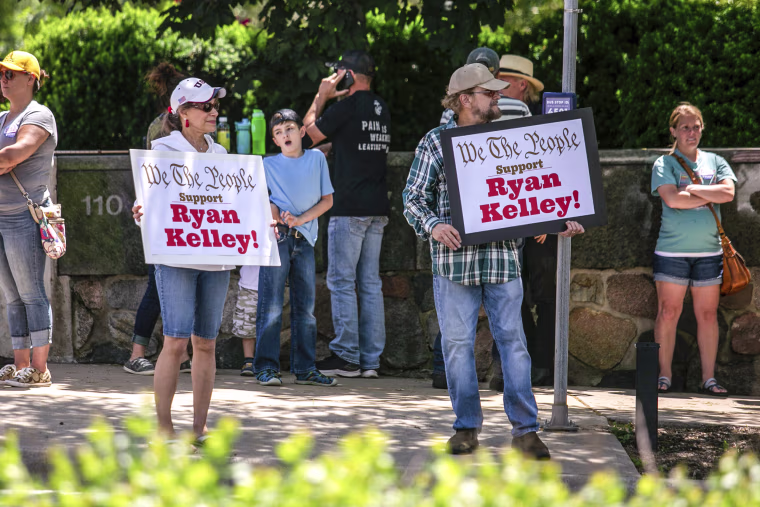Image: Supporters of Michigan gubernatorial candidate Ryan Kelly hold up signs as traffic passes by on Michigan Street while waiting for him to come out of the U.S. District Court in Grand Rapids, Mich., on June 9, 2022.