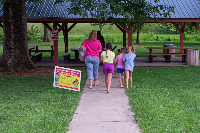 Image: Children follow as Christina Pinkerton and Shannon Bundridge take  food for the Summer Eats to the picnic area  in Kirksville, Mo., as on Aug. 16, 2022.