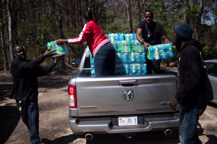 Image: Members of Operation Good distribute cases of water in an apartment complex in Jackson, Miss., on March 24, 2022.