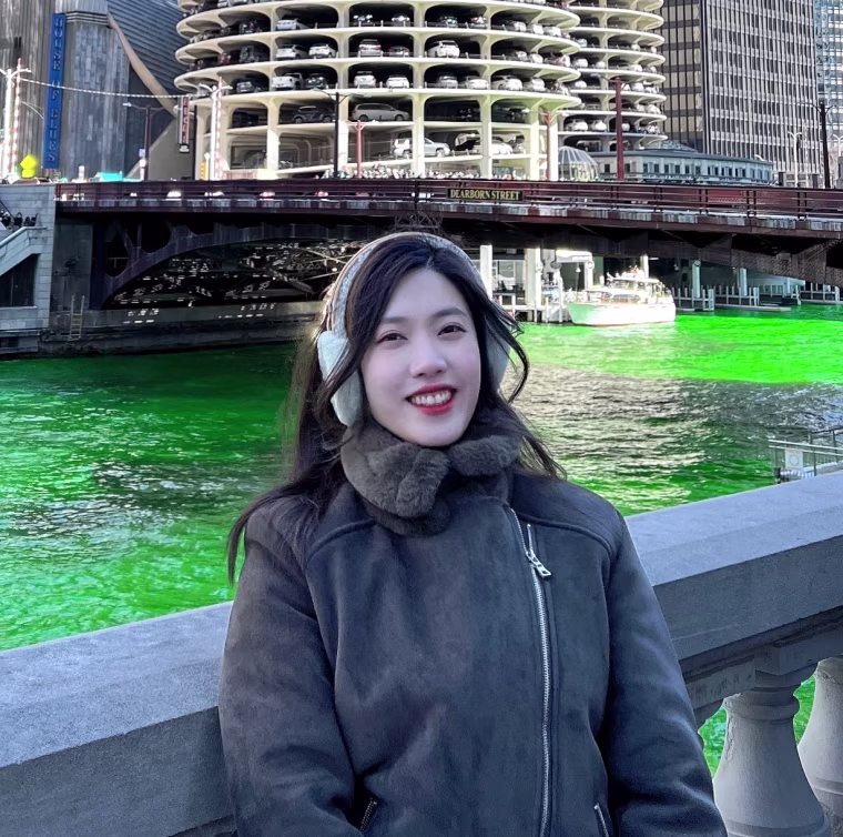 Jieun Kim, standing beside the Chicago River, which looks like it has been dyed green for St. Patrick's Day, with the Marina Towers behind her