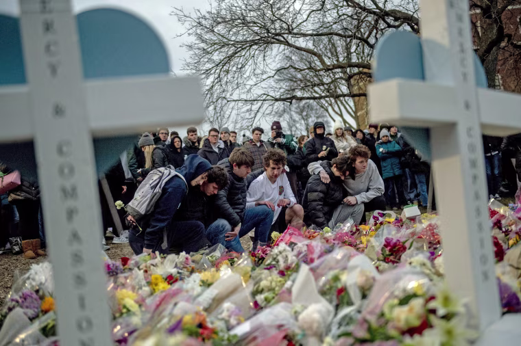Michigan State University students kneel at a memorial in East Lansing, Mich.