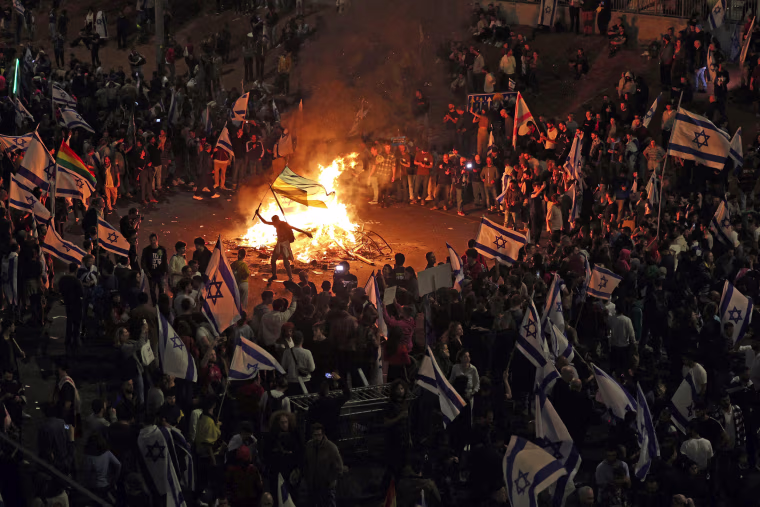 Protesters block a road and hold national flags as they gather around a bonfire during a rally against the Israeli government's judicial reform in Tel Aviv on March 27, 2023. 
