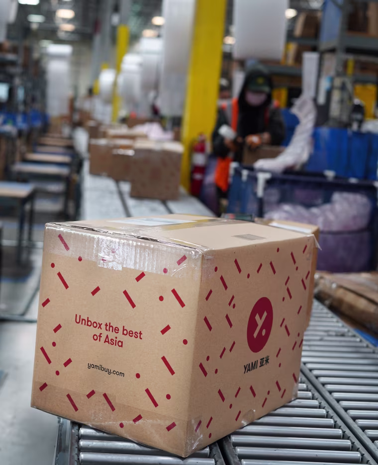 A box with a red logo on a conveyor belt in a warehouse.