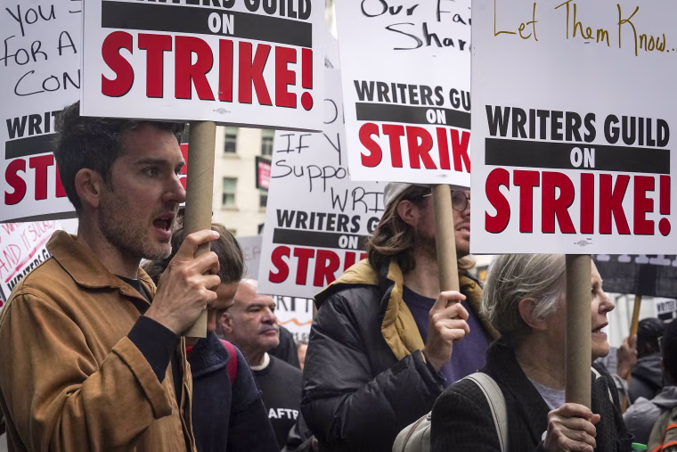 Striking writers hold signs as they march and picket calling for better wages, Tuesday, May 2, 2023, outside Peacock NewFront in New York.