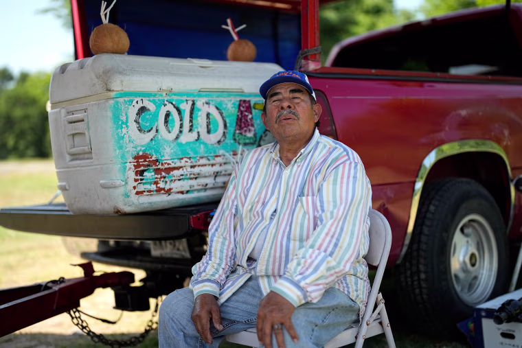 Andres Matamoros sits in the shade as he tries to keep cool while selling fresh fruit and cold coconuts in Houston on June 28, 2023.