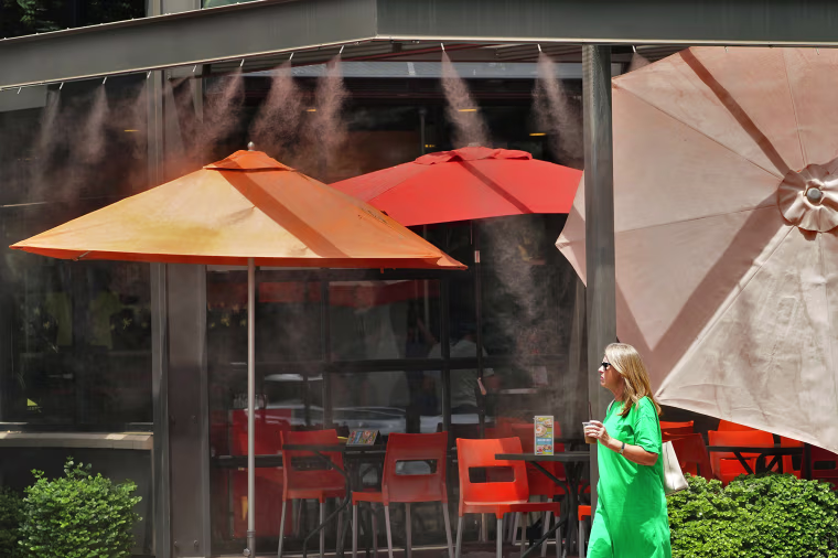A lady walks under misters outside a restaurant, Wednesday, July 12, 2023 in Gilbert Ariz. Even desert residents accustomed to scorching summers are feeling the grip of an extreme heat wave smacking the Southwest this week. Arizona, Nevada, New Mexico and Southern California are getting hit with 100-degree-plus temps and excessive heat warnings. (AP Photo/Matt York)