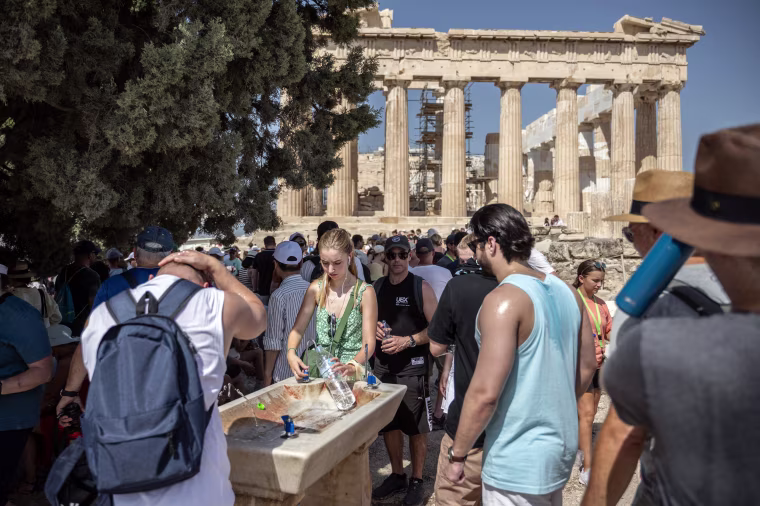Tourists cool off at a water fountain during their visit to the Parthenon Temple in Athens, Greece