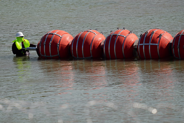 A worker helps deploy a string of large buoys to be used as a border barrier at the center of the Rio Grande near Eagle Pass, Texas, on July 11, 2023.