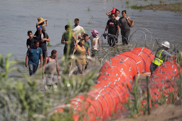 Migrants trying to enter the U.S. from Mexico approach the site where workers are assembling large buoys to be used as a border barrier along the banks of the Rio Grande in Eagle Pass, Texas, on July 11, 2023.