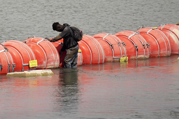 A migrant from Colombia stands at a floating buoy barrier as he looks to cross the Rio Grande from Mexico into the U.S., Monday, Aug. 21, 2023, in Eagle Pass, Texas.