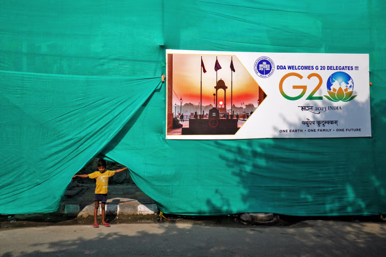 A boy pulls up plastic sheeting placed to screen a slum area alongside a road ahead of G20 Summit in New Delhi