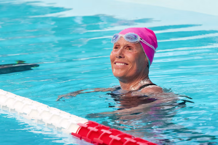 Diana Nyad smiles in a pool. She is wearing a pink swim cap.