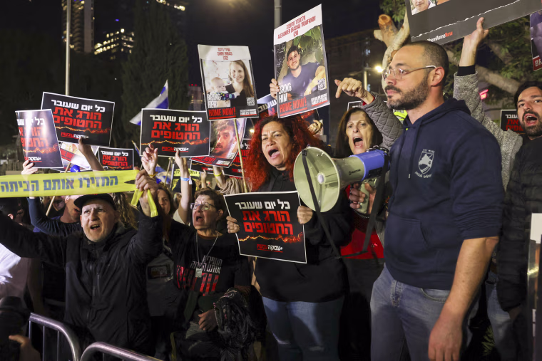 People hold sign, some with images of Israeli hostages, while protesting.