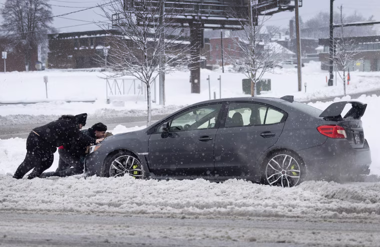 People help push a vehicle back onto the road after it became stuck in the snow in Des Moines, Iowa, on Tuesday.