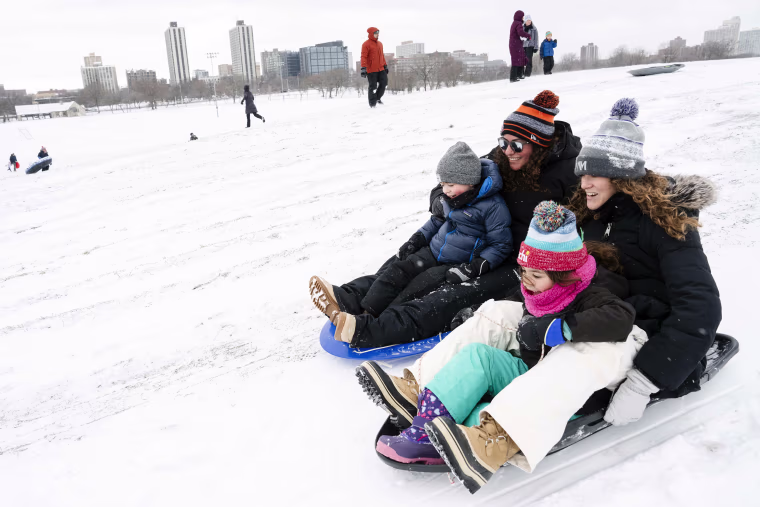 Allison Melowsky and wife Sarah Melowsky sled down Cricket Hill on Saturday with their kids Parker, 7, and Zane, 4, after a snowstorm in Chicago.