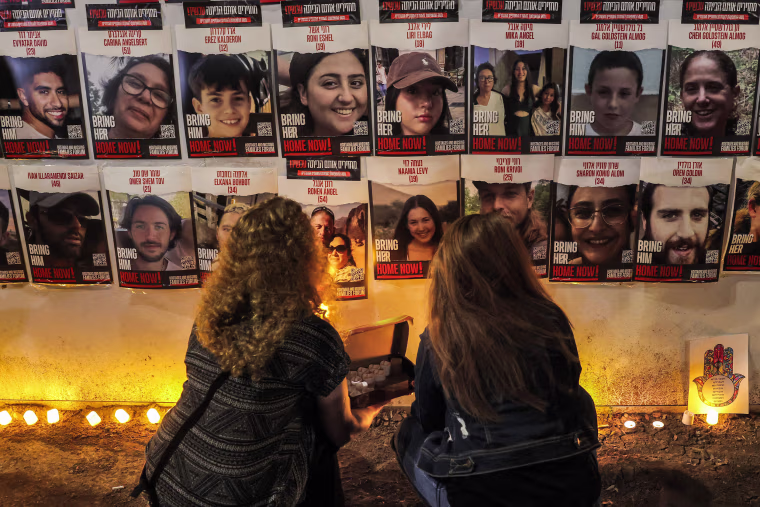 People light candles beneath a wall showing posters identifying hostages abducted by Palestinian militants during the October 7 attack, in Jerualem