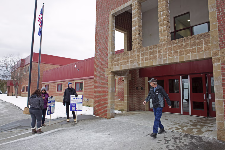 Supporters of President Joe Biden hold signs urging voters to "write-in Joe Biden" in the New Hampshire primary at Belmont High School on Jan. 22, 2024.