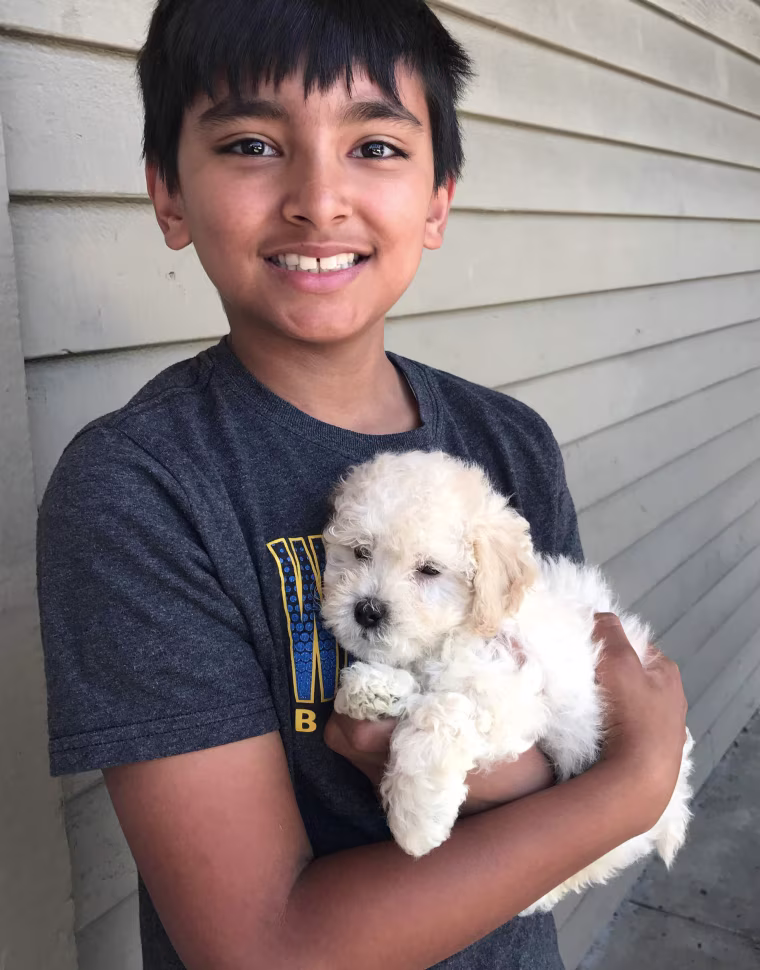 Childhood photo of Akul Dhawan smiling while holding a puppy.