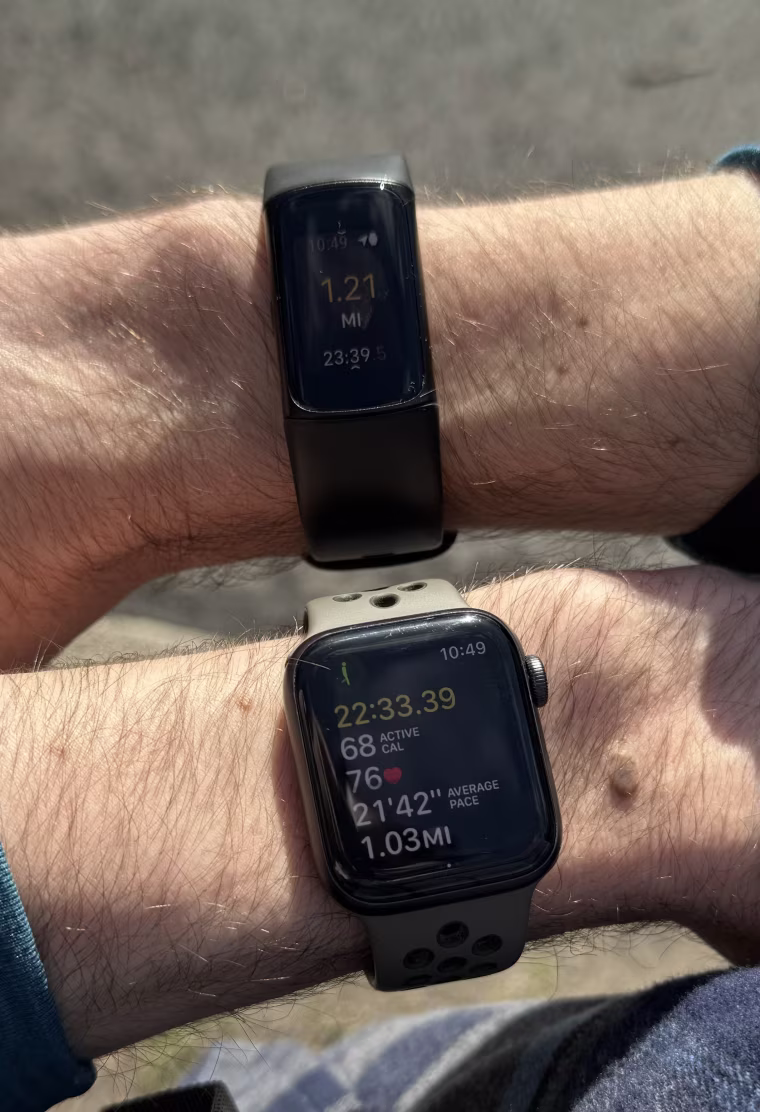 Close up shot of the Fitbit Charge 6 and Apple Watch SE screens on the left and right wrists of the writer.