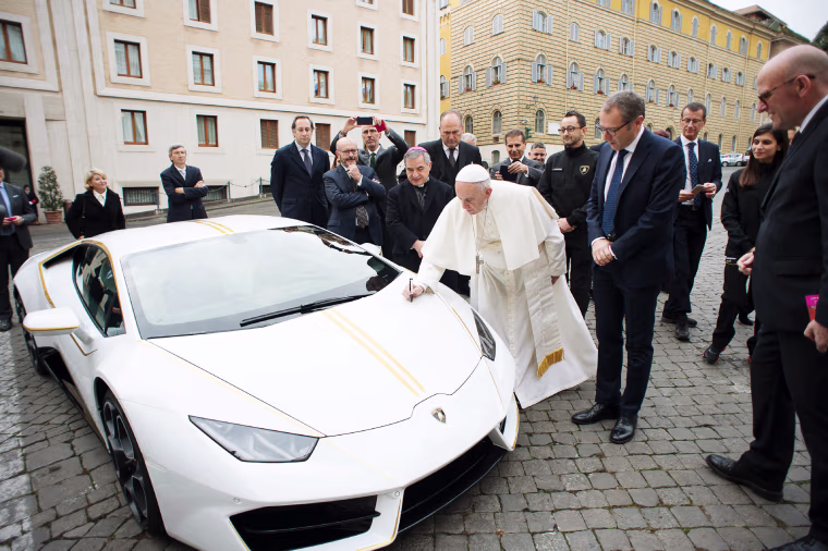 Pope Francis signs a Lamborghini Huracan received as a gift as Lamborghini CEO Stefano Domenicali, to the right of the pope, looks on.