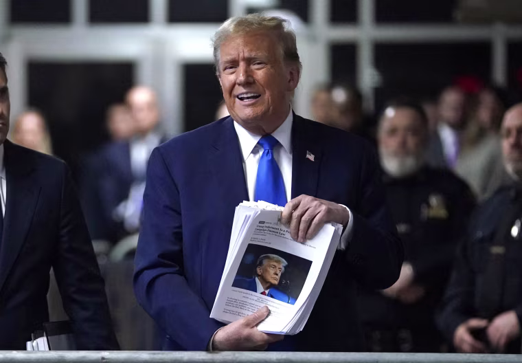 Former President Donald Trump holds news clippings as he leaves court for the day on April 18, 2024.