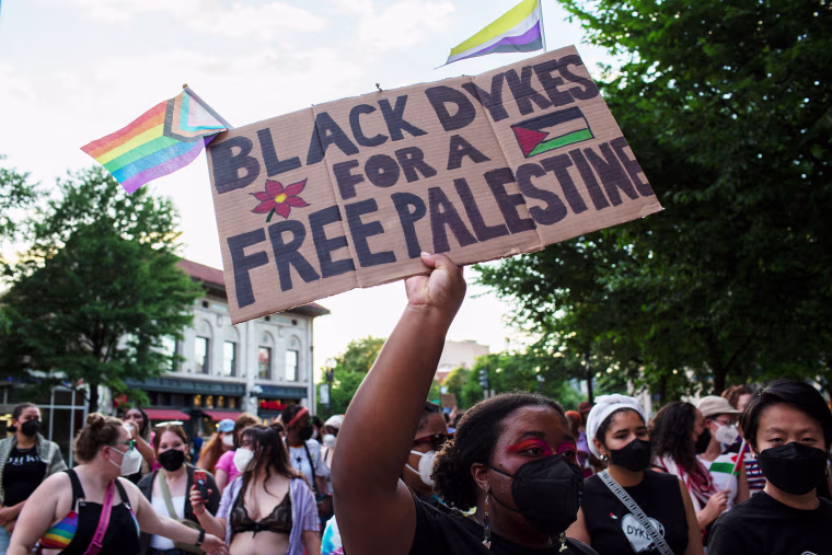 An activist holding a sign with "Black Dykes For A Palestine"