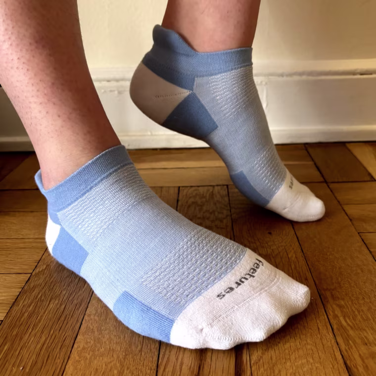 Malin wears blue socks with her back foot arched to show the design of the sock, including the tab and no-toe seam