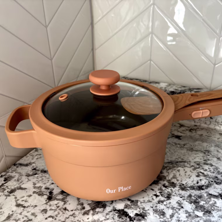 The Our Place Perfect Power Pot with the included vented glass lid on top and Beechwood spatula.