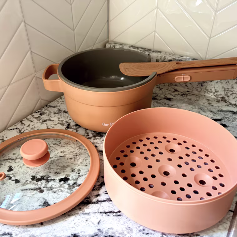 The Our Place Perfect Power Pot with its included accessories: a vented lid, steamer basket and nesting Beechwood spatula.