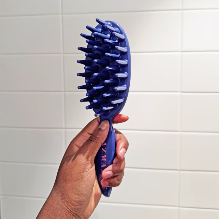 Woman holds a blue paddle brush in her hand at an angle to showcase the brush’s bristles.