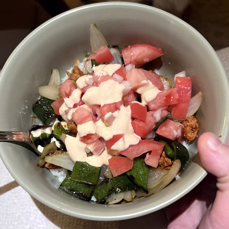 Burrito bowl with fresh tomato, green pepper, onion and an aioli over rice in a green bowl