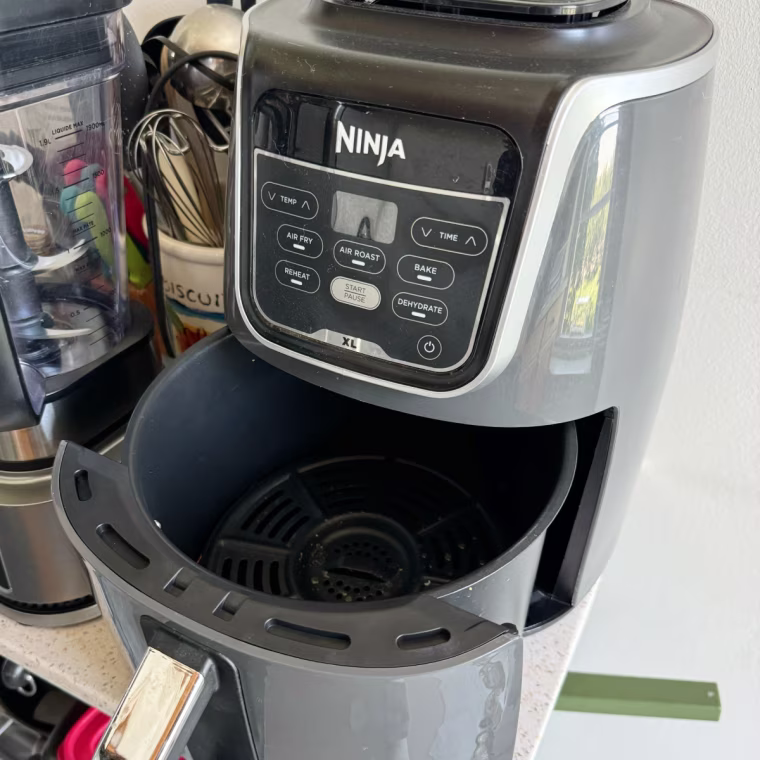 Ninja AF101 Air Fryer sitting on a kitchen counter with its basket open.