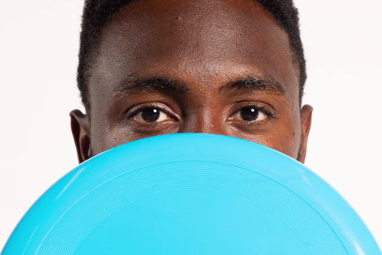 Marques Brownlee holding a blue frisbee in front of his face.