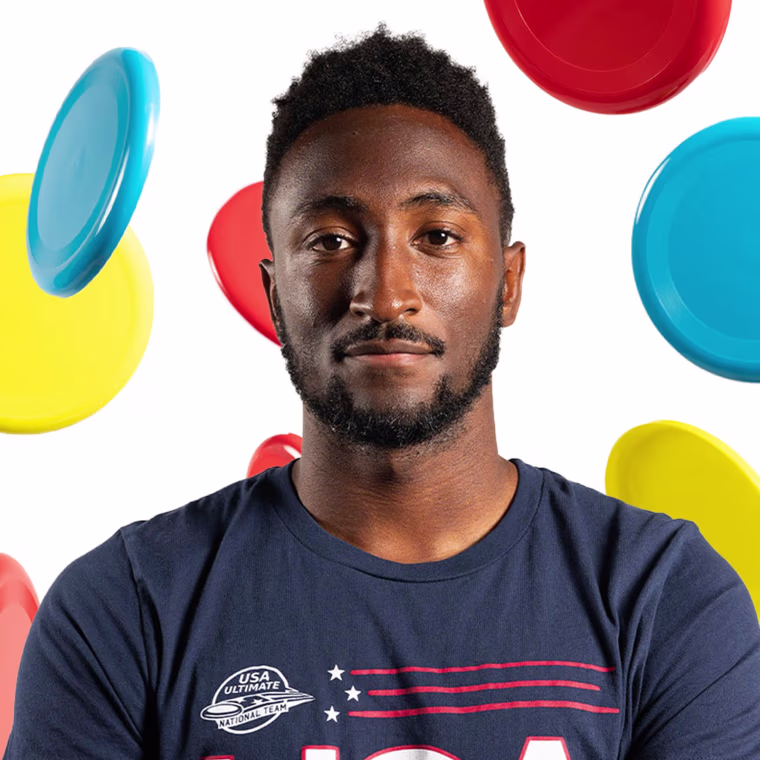 Marques Brownlee with his arms crossed with multicolored frisbees flying behind him. 