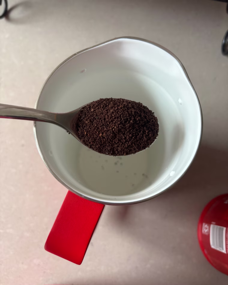 Man holding a spoonful of ground coffee above the Yeti French press.