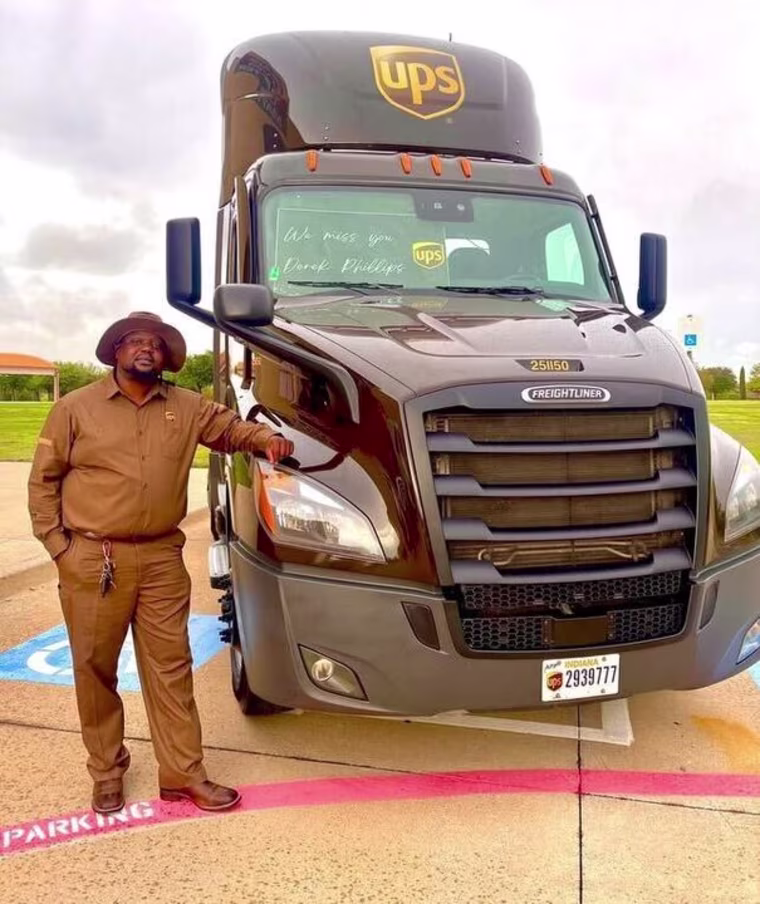Photo of man in UPS uniform leaning against the front of UPS truck