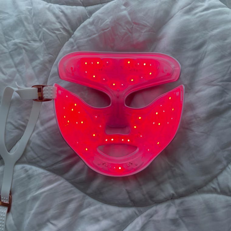 Three images of the DRx Spectralite Faceware Pro facedown on a white comforter with the first photo showing the red LED lights, the second photo showing the blue LED lights, and the third photo showing the combined red and blue LED light setting.