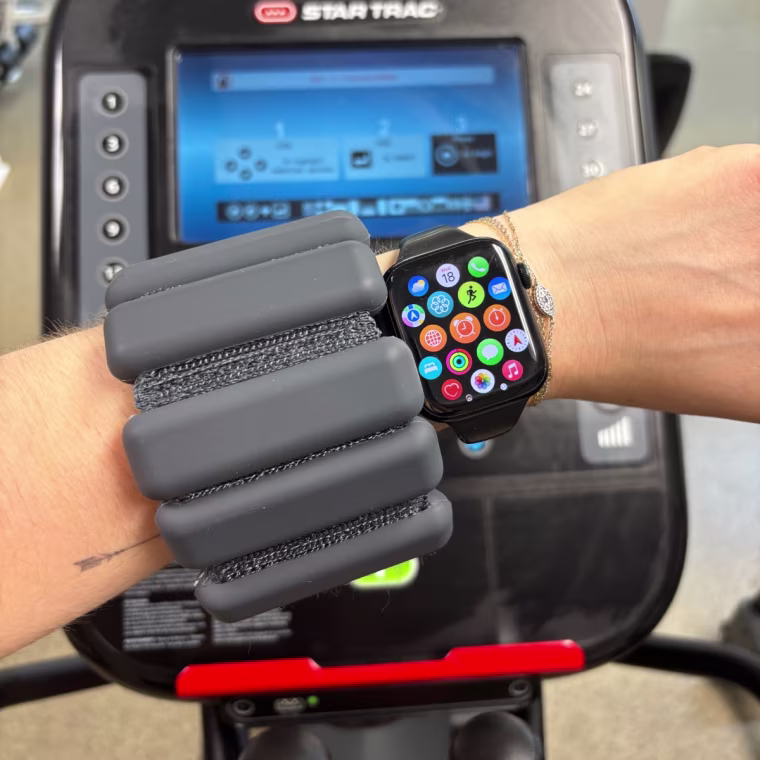 Woman’s arm in a gym with a black Bala Bangle and an Apple Watch on it.