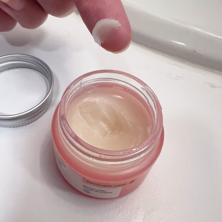 Woman scoops a tiny amount of Cosrx’s lip mask onto her finger.